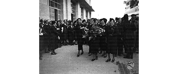 Napoli Accolto festosamente da giovani donne in divisa fascista, un gruppo di falangiste, tra cui Pilar Primo de Rivera, cammina, con mazzi di fiori in mano, lungo il molo a cui è attraccata la nave "Rex"