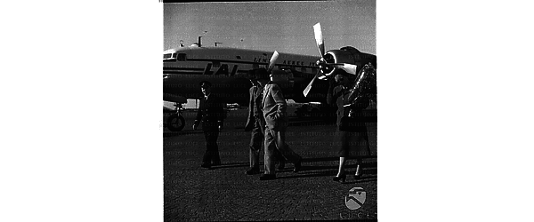 Lord e lady Jowitt, accompagnati da un uomo e da un assistente di volo della LAI, percorrono il piazzale di un aeroporto - Ciampino (?). Campo medio