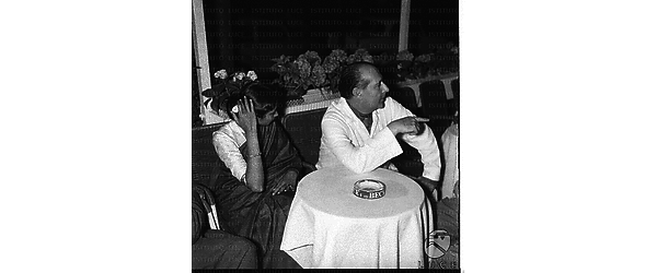 Roberto Rossellini e la moglie Sonali Das Gupta seduti ad un tavolino di un locale di via Veneto - piano americano