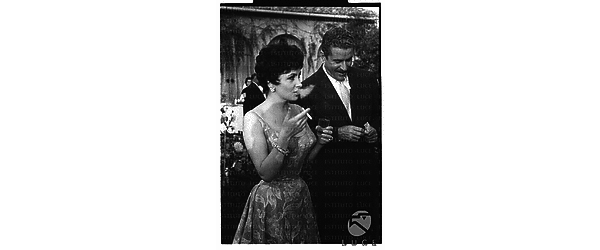 Gina Lollobrigida ripresa in occasione del ricevimento nella sua villa mentre fuma una sigaretta accanto ad Amedeo Nazzari - piano americano