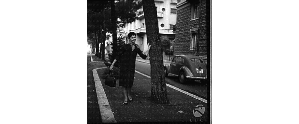 Una modella con un vestito elegante in posa in una aiuola vicino un albero. Campo medio