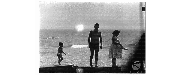 Un uomo ed bambino in costume ripreso in piedi sul molo di Santa Marinella, accanto una signora con prendisole - campo medio