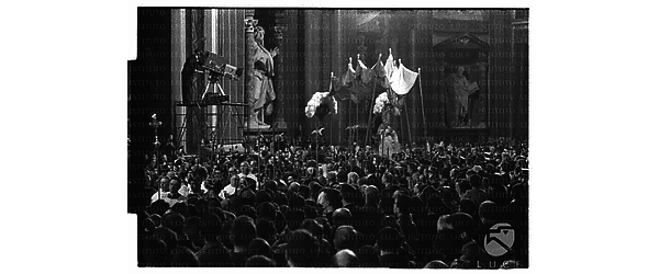 Il Papa passa lungo la navata della basilica di San Giovanni in Laterano affollata di fedeli sulla sedia gestatoria; sulla sinistra un cameraman riprende la scena - campo lungo